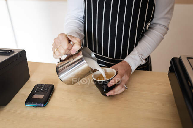 Midsection do proprietário do negócio fêmea que veste o avental, derramando o leite da espuma ao café. pequeno negócio café independente. — Fotografia de Stock