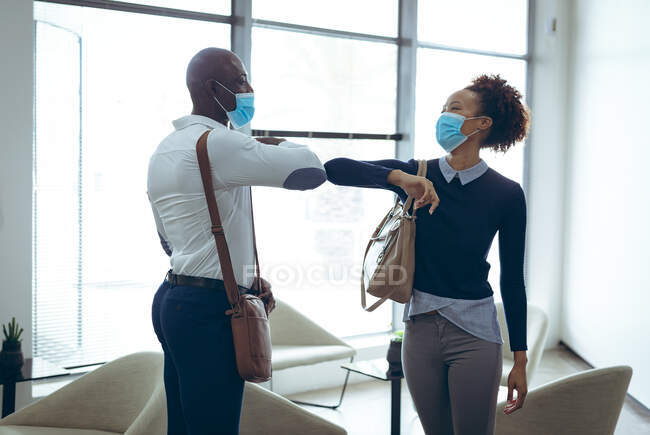 Deux collègues d'affaires masculins et féminins divers portant des masques faciaux et saluant avec des coudes. travailler dans un bureau moderne pendant la pandémie de coronavirus covid 19. — Photo de stock