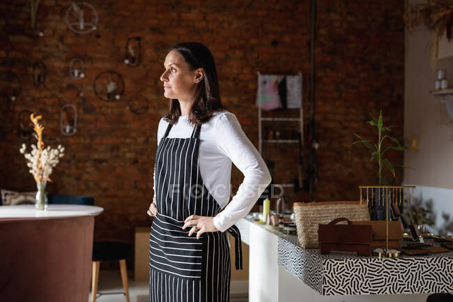 Caucasian female business owner wearing striped apron and looking out of window. small independent cafe business. — Stock Photo