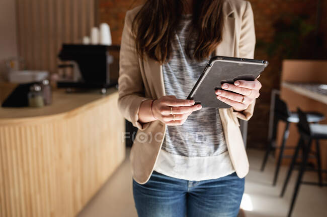 Midsection de mulher com cabelo longo em roupas casuais de pé, segurando tablet. pequeno negócio café independente. — Fotografia de Stock