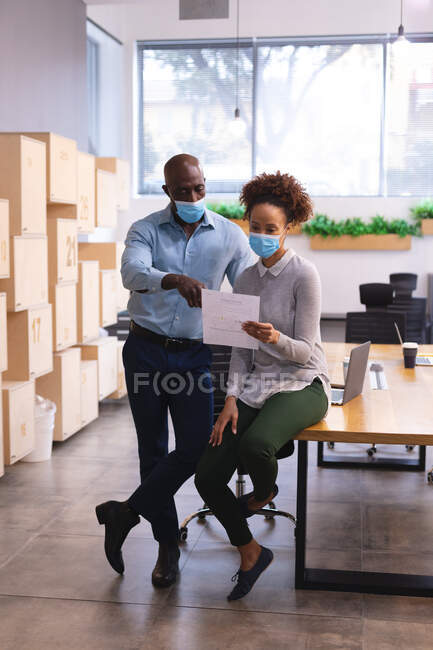 Two diverse male and female business colleagues wearing face masks and holding documents. work at a modern office during covid 19 coronavirus pandemic. — Stock Photo