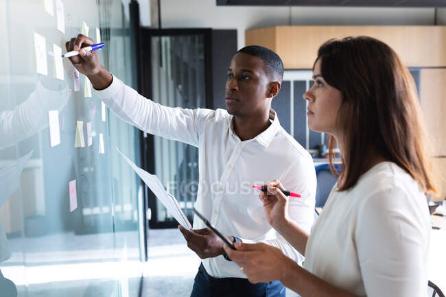 Diversi uomini d'affari e donne d'affari che scrivono su appunti su lavagna di vetro in un ufficio moderno. concetto di business e ufficio — Foto stock