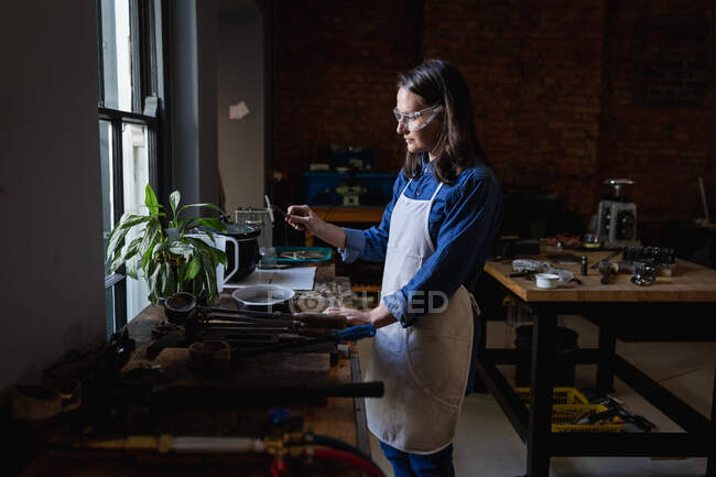 Кавказька жінка-ювелір, одягнена в фартух і окуляри, готує матеріали для ювелірних виробів. Незалежний ремісничий бізнес. — стокове фото