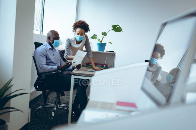 Two diverse business colleagues wearing face masks and discussing. work at a modern office during covid 19 coronavirus pandemic. — Stock Photo