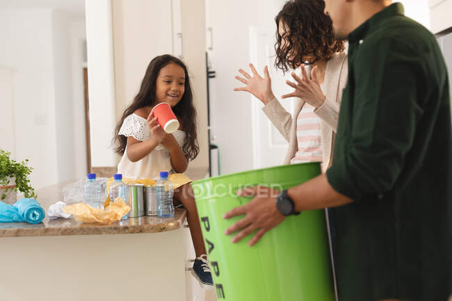 Feliz hija hispana y padres clasificando basura para su reciclaje en la cocina. en casa en aislamiento durante el bloqueo de cuarentena. - foto de stock