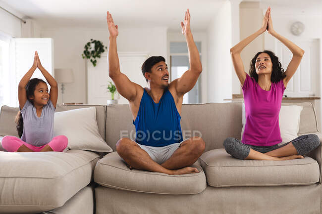 Lächelnde hispanische Tochter und Eltern, die auf der Couch im Wohnzimmer Yoga praktizieren. Zuhause in Isolation während der Quarantäne. — Stockfoto