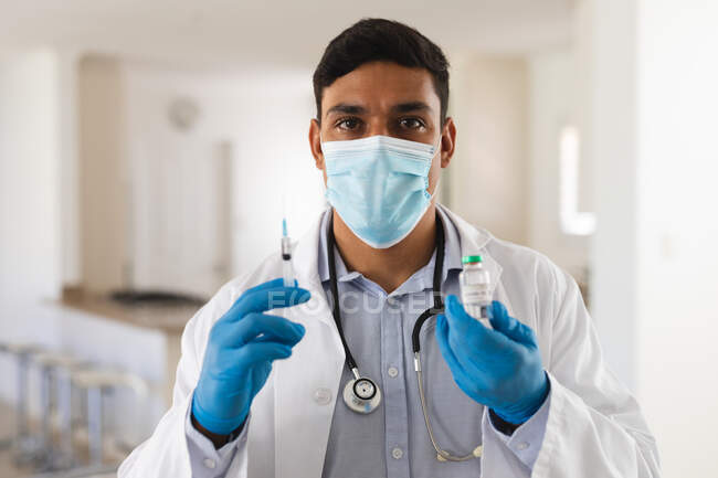 Portrait of hispanic male doctor wearing face mask holding covid 19 vaccination. medical and healthcare services during coronavirus covid 19 pandemic. — Stock Photo