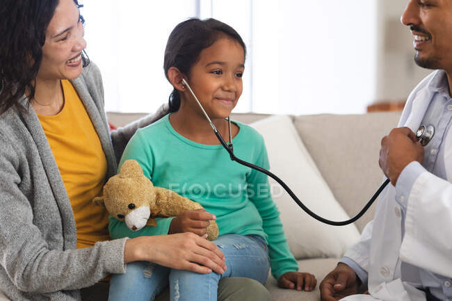 Médico hispânico feliz e paciente menina com a mãe brincando com estetoscópio durante a visita domiciliar. serviços médicos e de saúde. — Fotografia de Stock