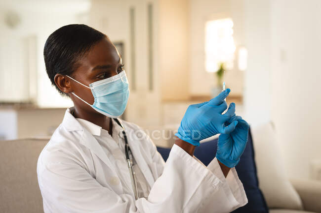 Médica afro-americana em máscara facial e luvas preparando vacinação vívida. serviços médicos e de saúde durante a pandemia do coronavírus covid 19. — Fotografia de Stock