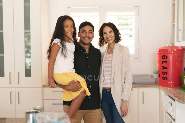 Portrait de heureuse fille hispanique et parents debout dans la cuisine souriant. à domicile en isolement pendant le confinement en quarantaine. — Photo de stock