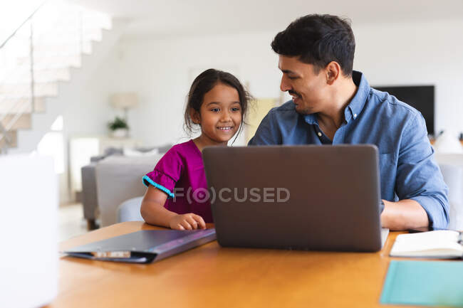 Sonriendo padre hispano e hija sentados en la sala de estar usando un ordenador portátil juntos. familia pasar tiempo juntos en casa. - foto de stock