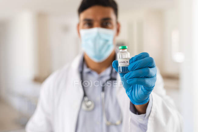 Portrait d'un médecin hispanique portant un masque facial contenant un flacon du vaccin covide 19. services médicaux et de santé pendant une pandémie de coronavirus covid 19. — Photo de stock