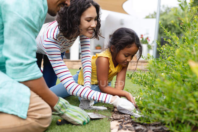 Smiling hispanic mother, father and daughter gardening, kneeling and planting in flower bed. family spending time together at home. — Stock Photo