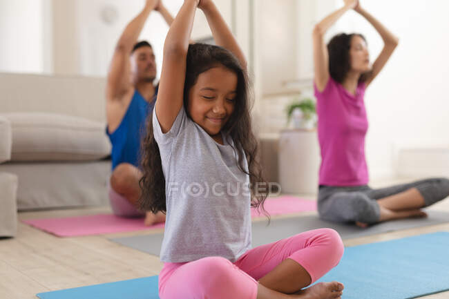 Lächelnde hispanische Tochter und Eltern, die im Wohnzimmer Yoga praktizieren. Zuhause in Isolation während der Quarantäne. — Stockfoto