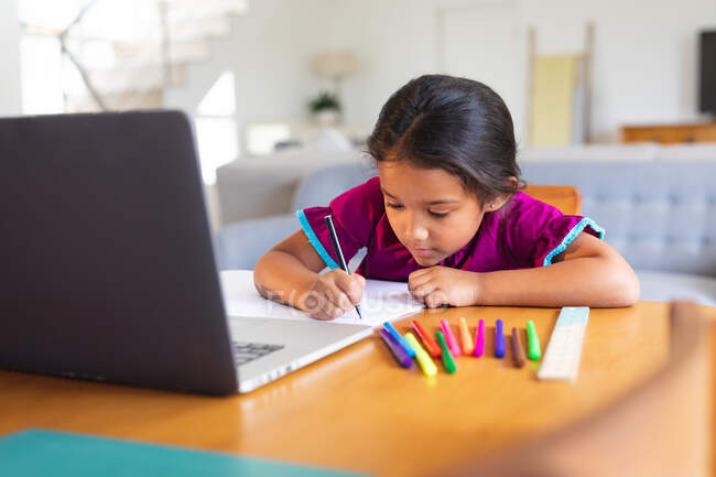 Счастливая латиноамериканка, сидящая за кухонным столом и занимающаяся школьной работой с ноутбуком. счастливая семья дома. — стоковое фото