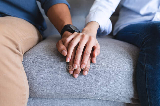 Hands of happy couple sitting on couch holding hands in living room. spending time together at home. — Stock Photo