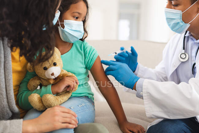 Врач-латиноамериканец проводит ковидовую вакцинацию дочери пациента с матерью в масках для лица. медицинские и медицинские услуги во время пандемии коронавируса. — стоковое фото