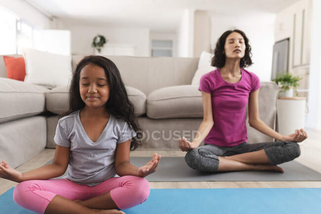 Lächelnde hispanische Mutter und Tochter beim Meditieren im Wohnzimmer. Zuhause in Isolation während der Quarantäne. — Stockfoto