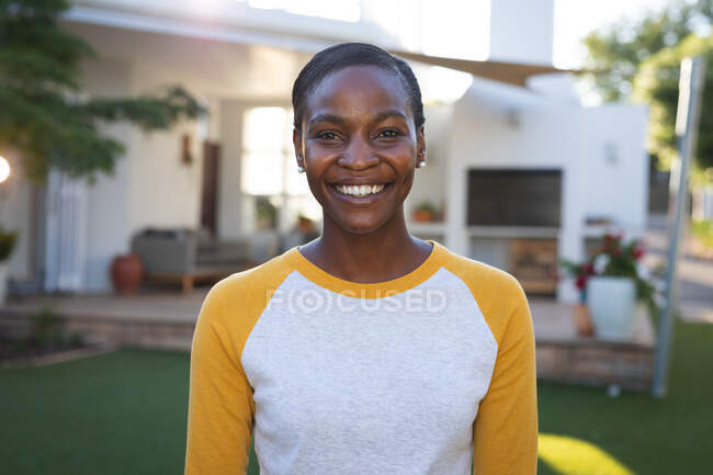 Retrato de mulher americana africana feliz em pé no jardim sorrindo para câmera, casa no fundo. passar tempo livre em casa. — Fotografia de Stock