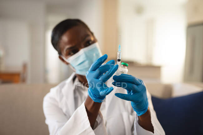 Doctora afroamericana en mascarilla facial y guantes preparando la vacunación covid. servicios médicos y sanitarios durante la pandemia de coronavirus covid 19. - foto de stock