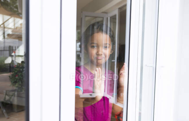 Hispanisches Mädchen, das mit den Händen auf Glas am Fenster steht, hinausblickt und ein trauriges Gesicht macht. Freizeit zu Hause. — Stockfoto