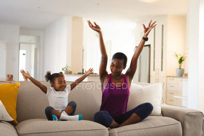 Mãe americana africana feliz e filha praticando ioga, sentado no sofá na sala de estar. família passar tempo juntos em casa. — Fotografia de Stock