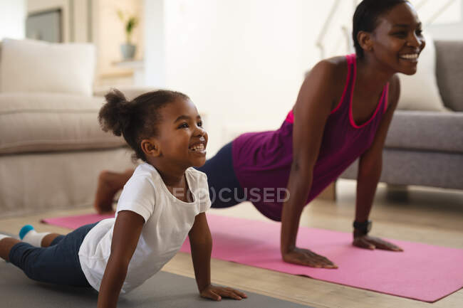 Mère et fille afro-américaine souriantes pratiquant le yoga, allongées sur des nattes qui s'étirent. passer du temps ensemble à la maison. — Photo de stock