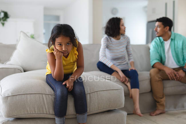Грустная латиноамериканская дочь, сидящая на диване с матерью и отцом, спорящими позади. семья проводит время вместе дома. ad — стоковое фото