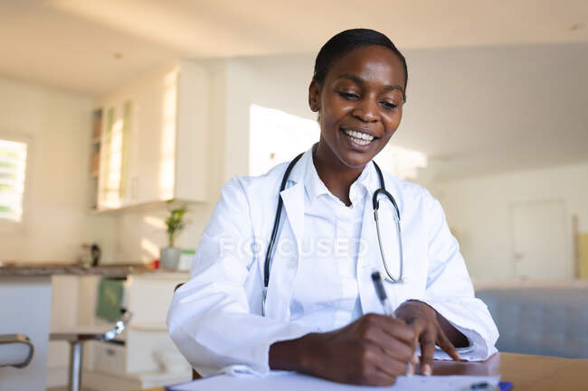 Lächelnde afrikanisch-amerikanische Ärztin, die während eines Videotelefonats spricht und Notizen macht. Telemedizin, medizinische Online-Dienste und Gesundheitsdienste. — Stockfoto