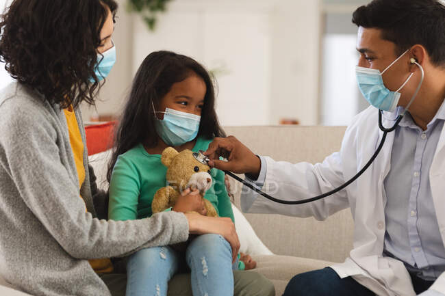 Hispanische Arzt mit Stethoskop zu Hause von Mutter und Tochter Patientin, tragen Gesichtsmasken. Medizinische und Gesundheitsdienste während der Coronavirus-Pandemie 19. — Stockfoto
