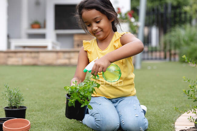 Smiling hispanic girl gardening, kneeling and watering plant in pot. family spending time together at home. — Stock Photo