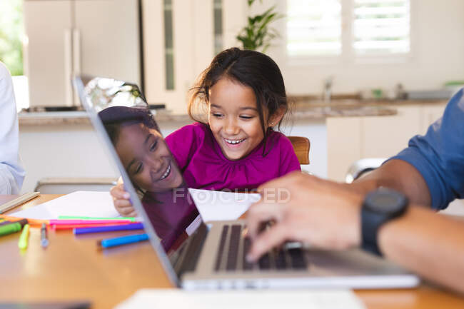 Sonriente hija hispana sentada en la cocina haciendo el trabajo escolar con el padre usando el portátil en primer plano. familia pasar tiempo juntos en casa. - foto de stock