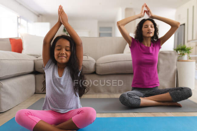 Lächelnde hispanische Mutter und Tochter, die im Wohnzimmer Yoga praktizieren. Zuhause in Isolation während der Quarantäne. — Stockfoto