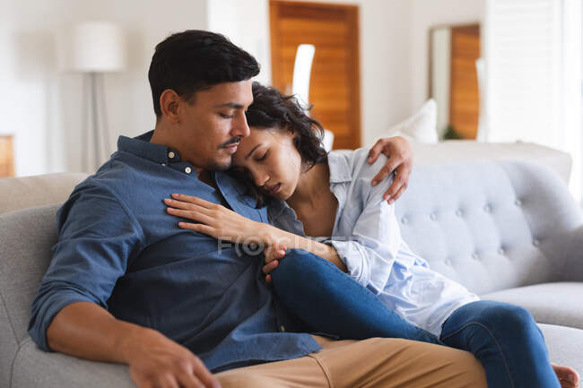 Trauriges hispanisches Paar, das auf der Couch im Wohnzimmer sitzt und sich umarmt. Zeit gemeinsam zu Hause verbringen. — Stockfoto