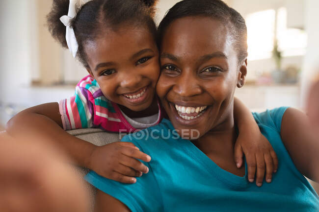 Mère et fille afro-américaine souriante se relaxant sur le canapé, prenant selfie. passer du temps ensemble à la maison. — Photo de stock
