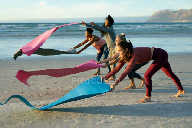 Gruppe verschiedener Freundinnen, die Yoga praktizieren und Matten am Strand auslegen. gesunder aktiver Lebensstil, Fitness und Wohlbefinden im Freien. — Stockfoto