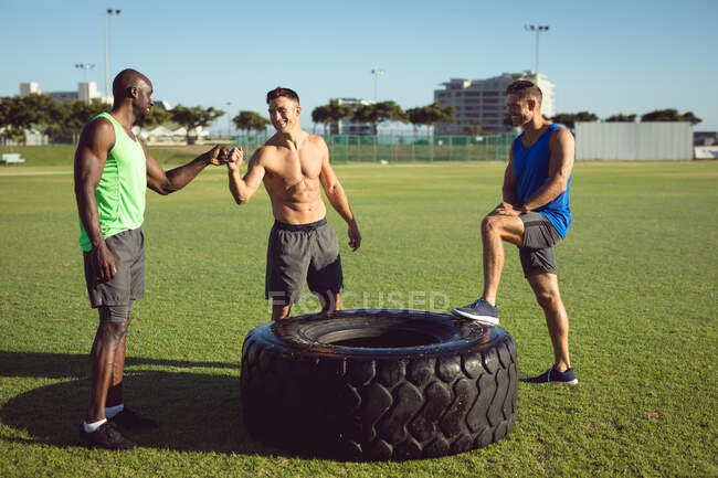 Diverse group of happy shirtless men exercising outdoors, taking a break talking and bumping fists. healthy active lifestyle, cross training for fitness. — Stock Photo