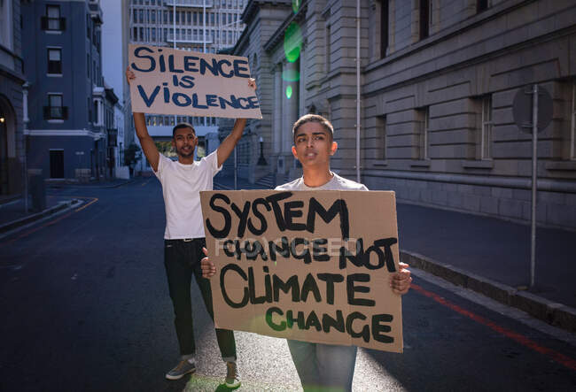 Deux amis de race mixte portant des panneaux de protestation peints à la main avec des slogans marchant dans la rue de la ville. Manifestants pour l'égalité des droits et la justice en ville. — Photo de stock