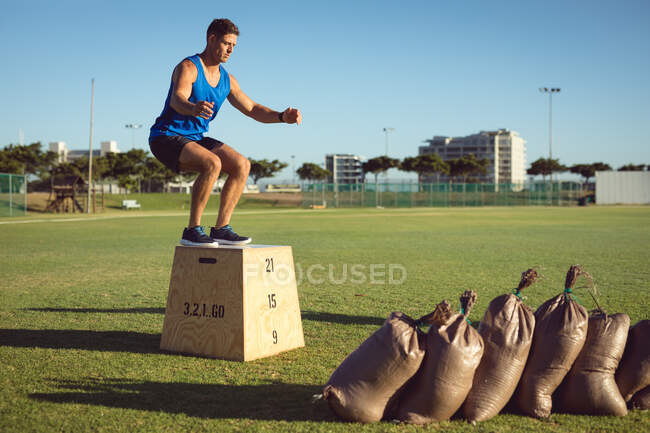 Ajuste hombre caucásico ejercicio al aire libre saltar a la caja. estilo de vida activo saludable, entrenamiento cruzado para fitness. - foto de stock
