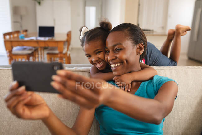 Lächelnd entspannen sich Mutter und Tochter auf der Couch und machen ein Selfie. Familie verbringt Zeit zu Hause. — Stockfoto