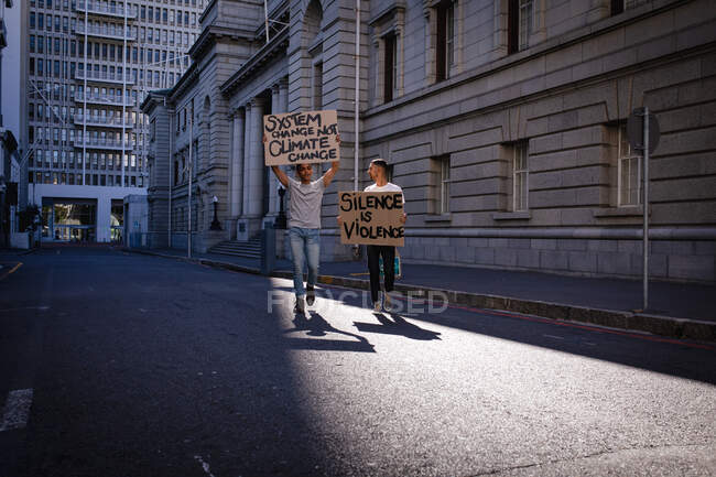 Two mixed race male friends carrying hand painted protest signs walking in city street. equal rights and justice protestors demonstrating in city. — Stock Photo