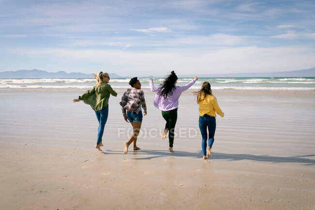Grupo feliz de amigas divertidas se divertindo, andando ao longo da praia. férias, liberdade e lazer ao ar livre. — Fotografia de Stock