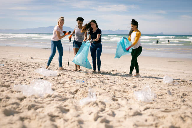 Diverso grupo de mujeres caminando por la playa, recogiendo basura de plástico. voluntarios de conservación ecológica, limpieza de la playa. - foto de stock