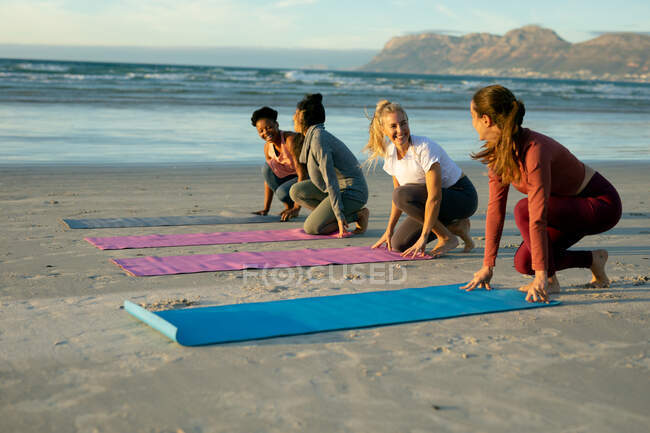 Groupe d'amies diverses pratiquant le yoga, posant des nattes à la plage. mode de vie sain et actif, forme physique extérieure et bien-être. — Photo de stock