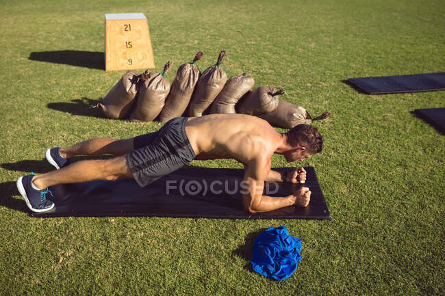 Hombre caucásico musculoso sin camisa haciendo ejercicio al aire libre, haciendo tablón. estilo de vida activo saludable, entrenamiento cruzado para fitness. - foto de stock