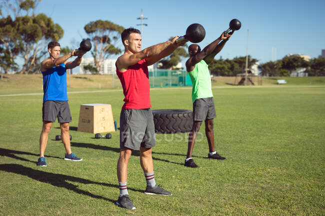 Diverso gruppo di uomini muscolosi che esercitano con campane del bollitore all'aperto. sano stile di vita attivo, cross training per il concetto di fitness. — Foto stock