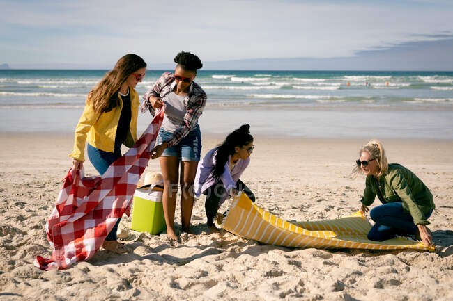 Feliz grupo de diversas amigas poniendo mantas en la playa. vacaciones, libertad y tiempo libre al aire libre. playa ho abajo mantas - foto de stock