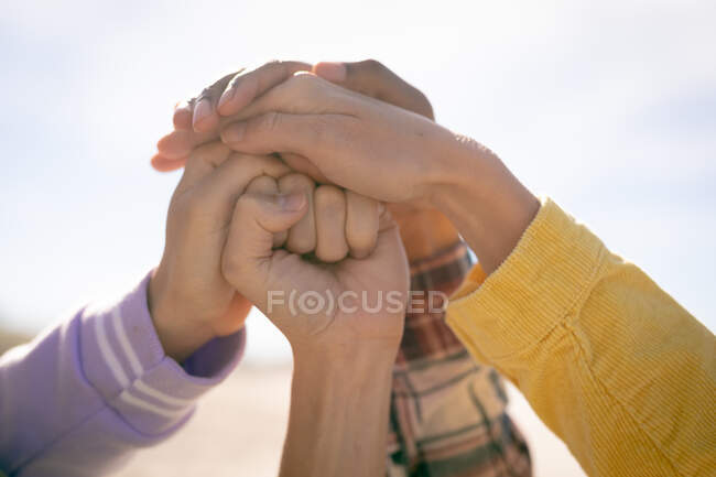 Manos de diverso grupo de mujeres apilando las manos contra el cielo azul. amigas unidas en la playa. - foto de stock