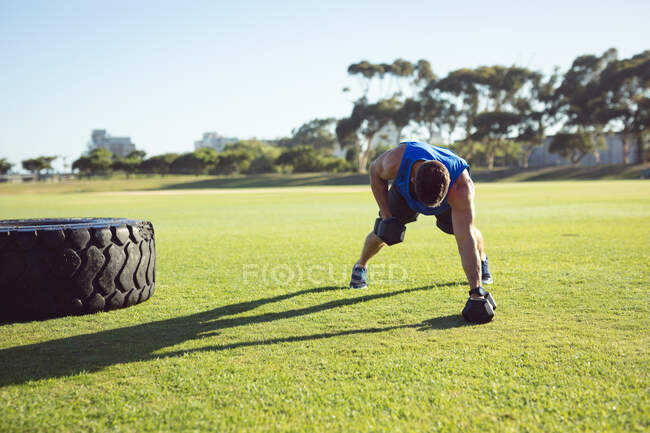Белый американский мускулистый человек, тренирующийся на улице с гантелями. здоровый активный образ жизни, кросс тренировки для фитнеса. — стоковое фото