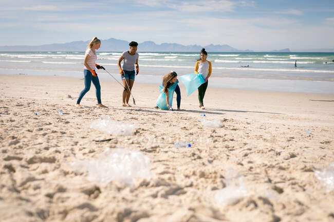 Разнообразная группа женщин, идущих вдоль пляжа, собирающих мусор. волонтеры по охране окружающей среды, уборка пляжа. — стоковое фото